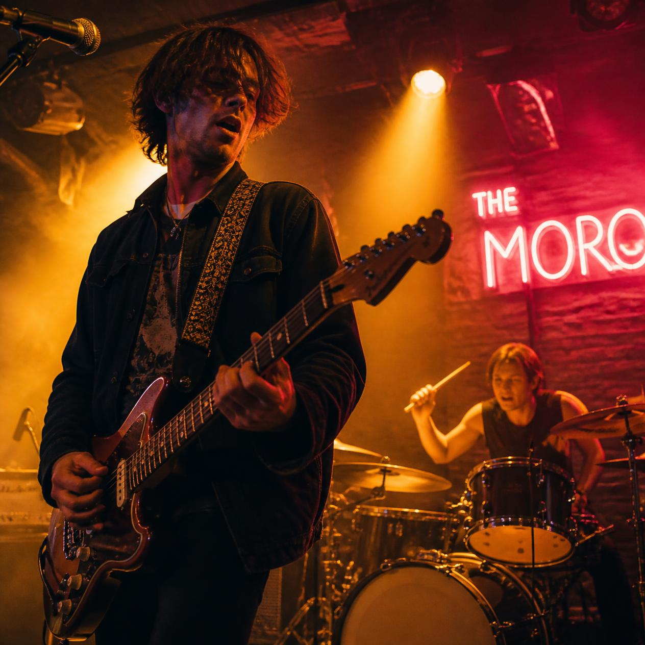 Local indie band performing live on stage under warm spotlights and neon glow in an intimate music venue